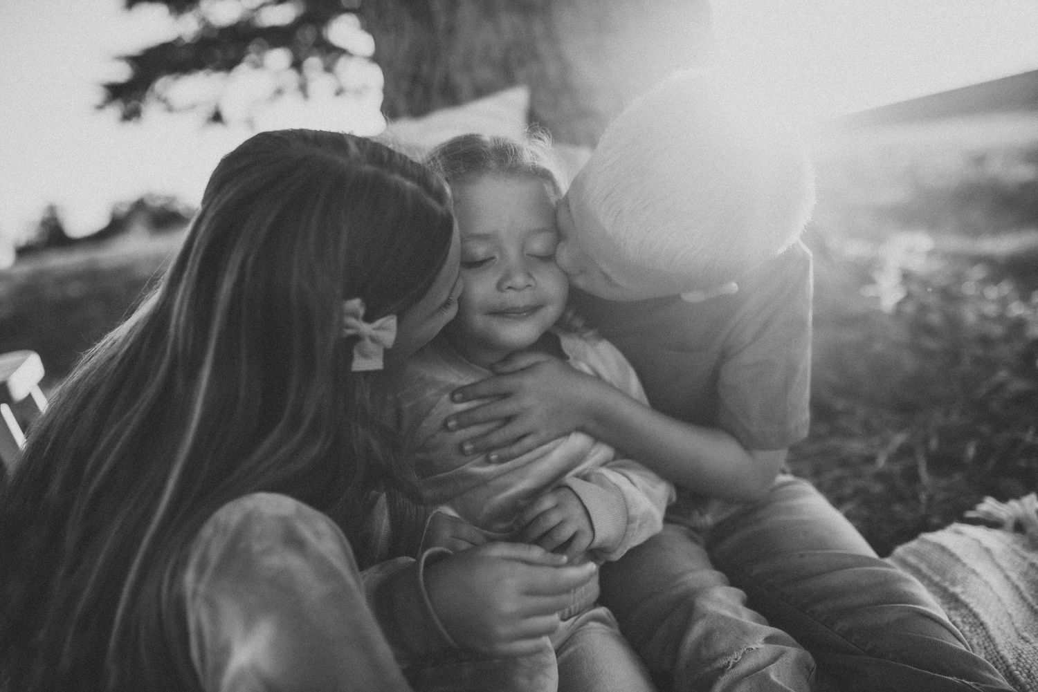 A candid black and white family moment captured during sunset with warm embraces and joyful expressions.