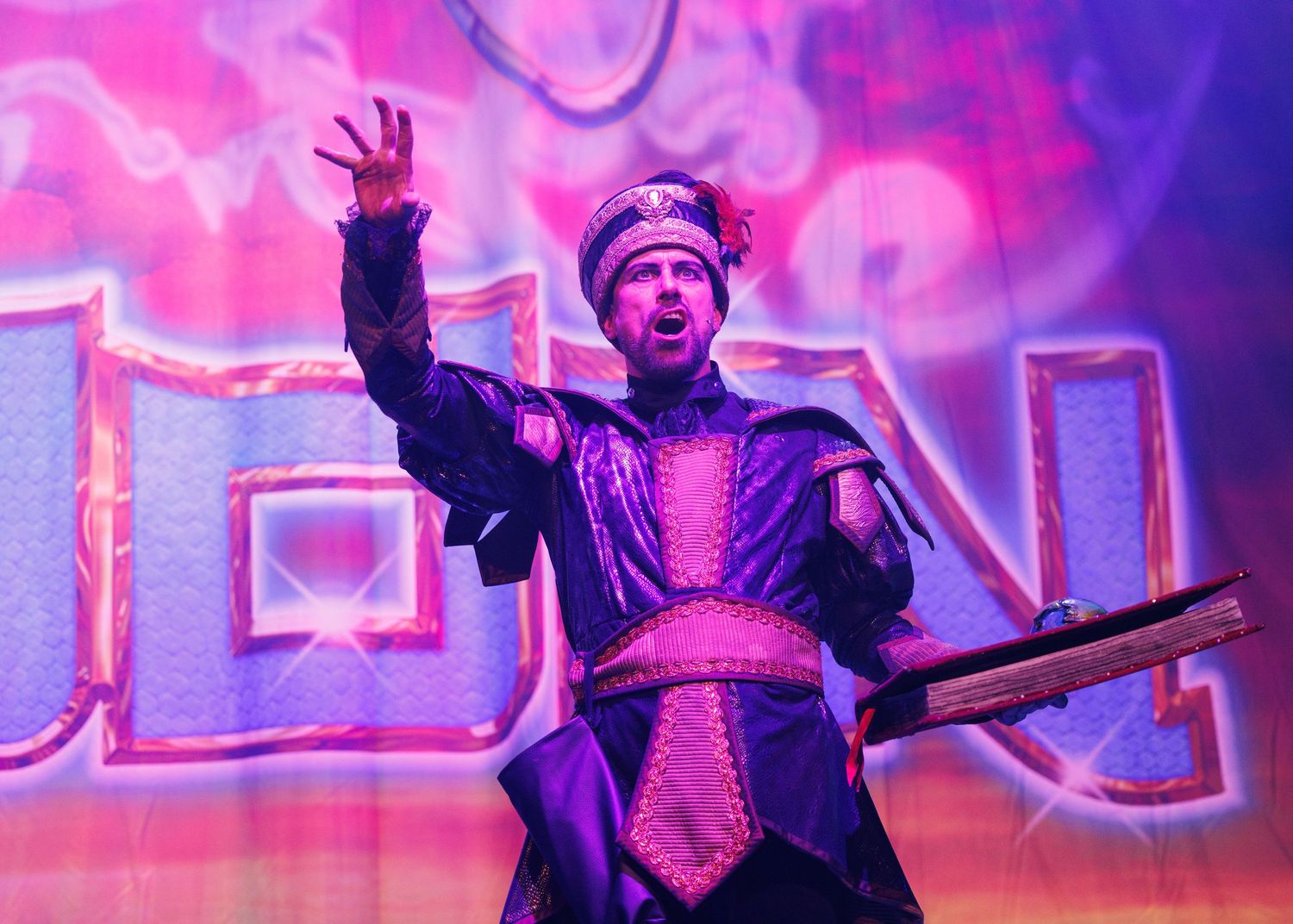 Performers on stage in dramatic poses under vibrant pink and purple theatrical lighting during a live show.