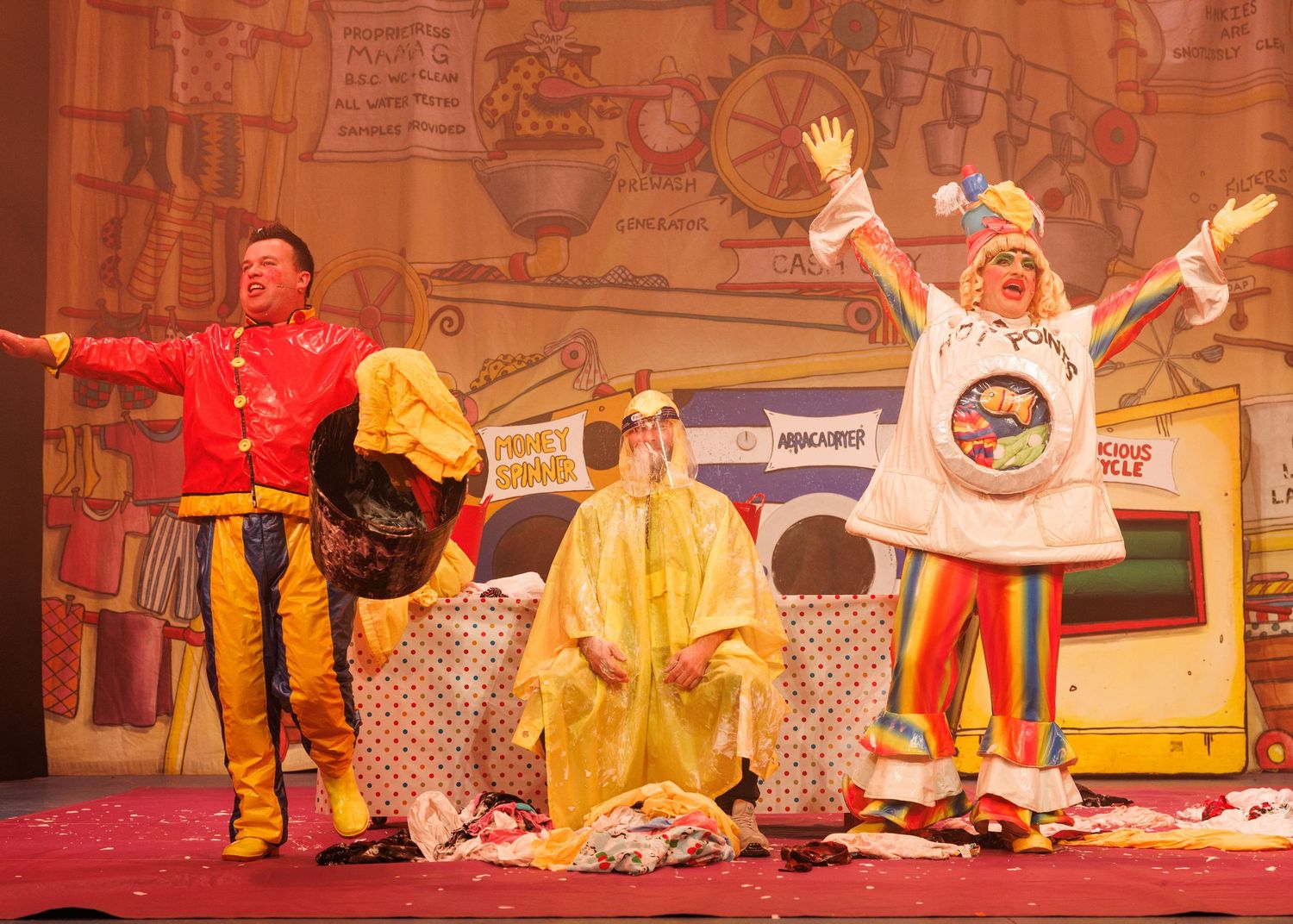 Theater performers in colorful costumes dance and gesture dramatically on a decorated stage during a musical performance.