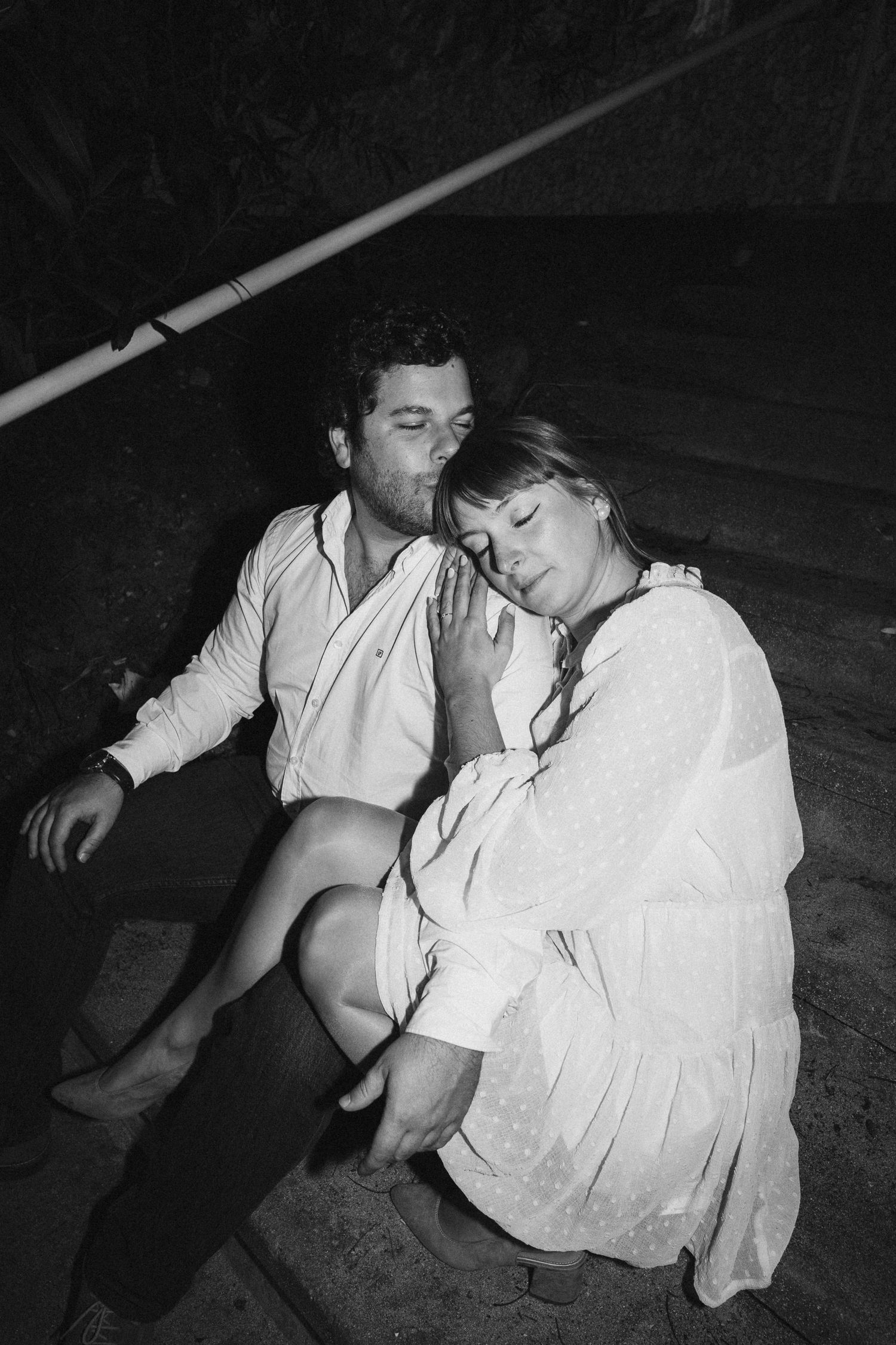 A black and white photo sequence shows two people in white clothing sitting close together on the ground.
