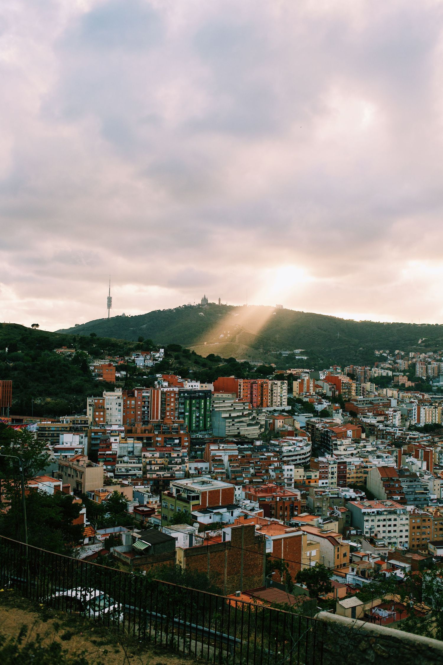 Panoramic cityscape view of densely packed buildings on hillside under cloudy sky during sunset.