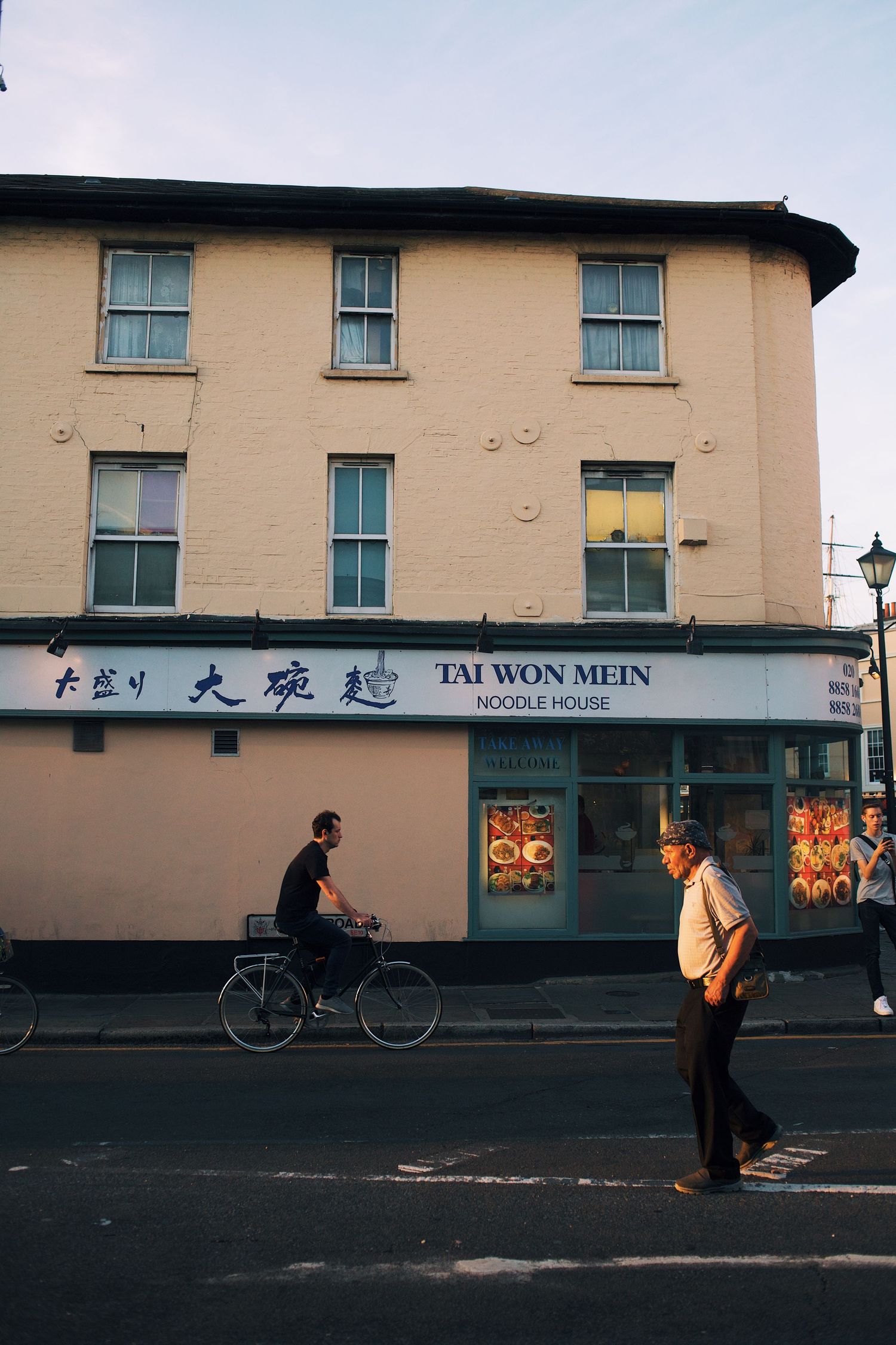 A panoramic view of a Chinese restaurant storefront with pedestrians walking past at dusk.