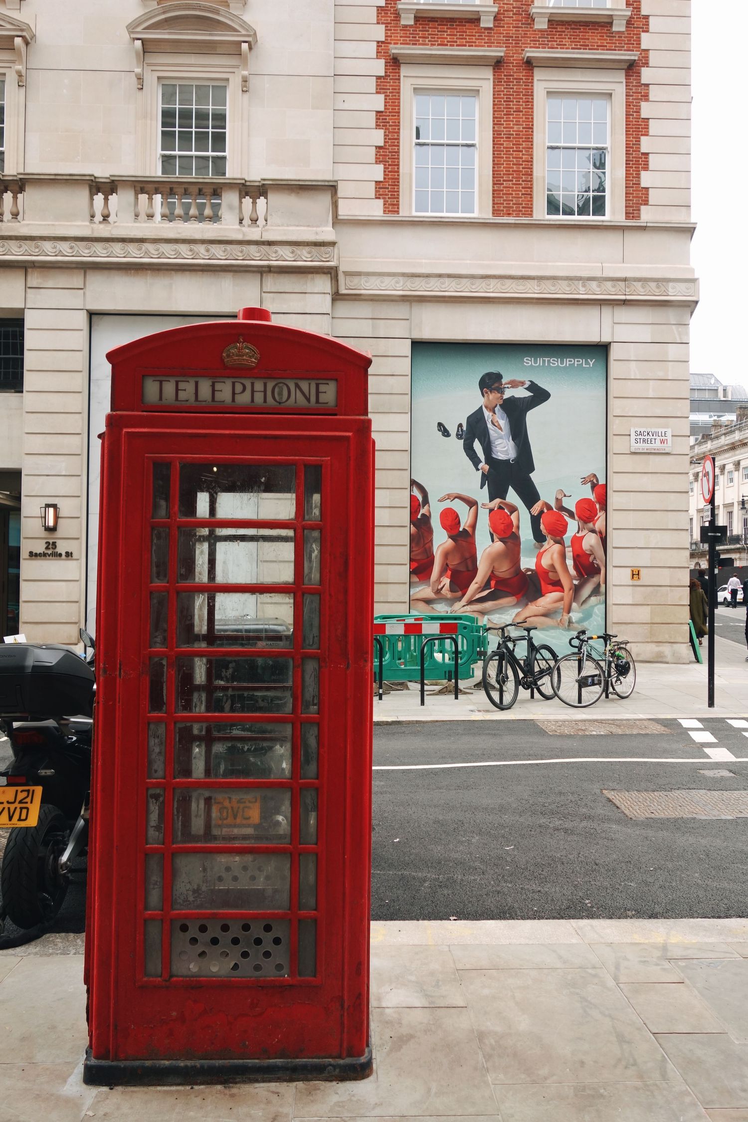 A row of iconic red British telephone booths stand against a light-colored building facade in an urban setting.
