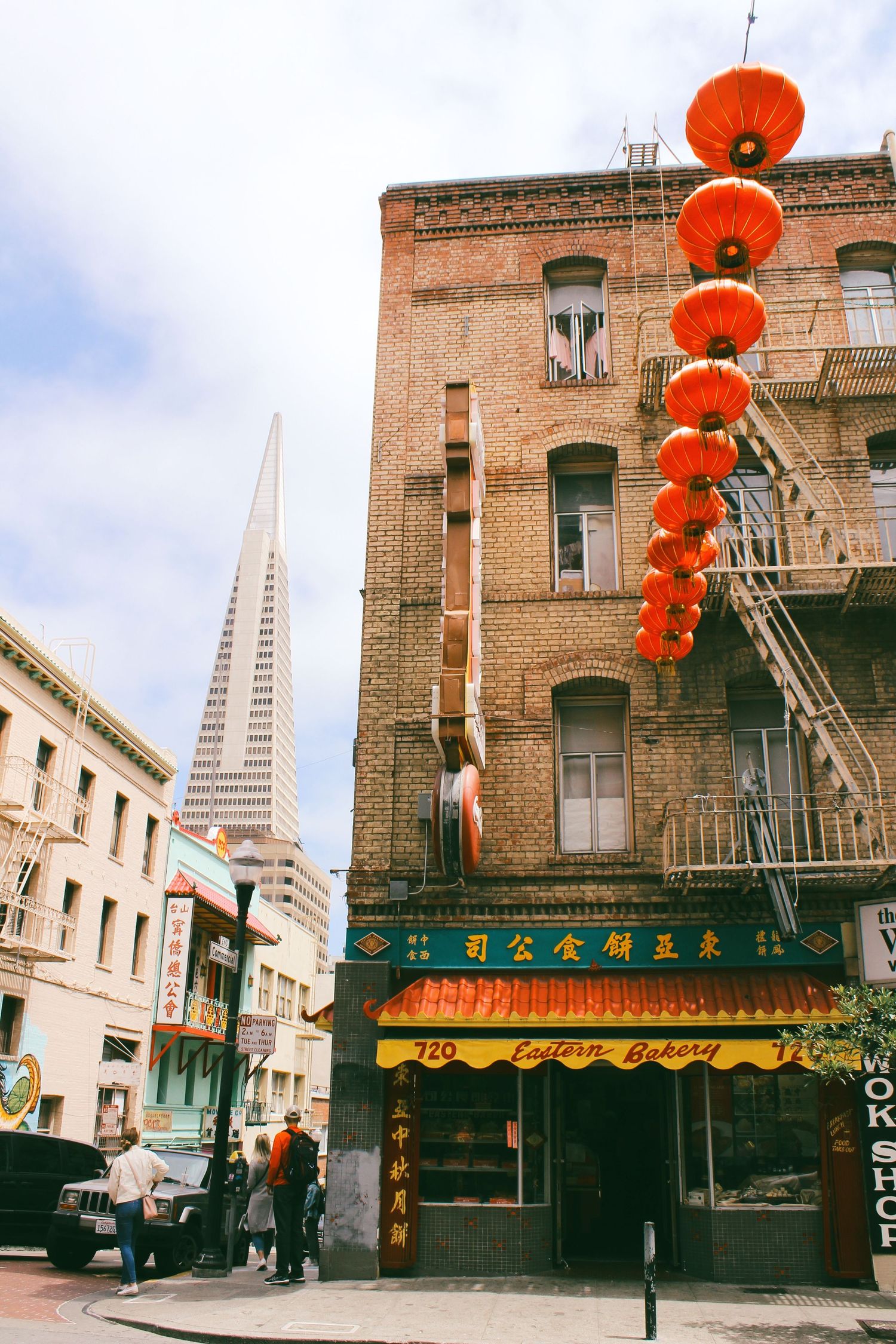 Red lanterns hang outside a brick building in San Francisco's Chinatown with the Transamerica Pyramid visible in background.