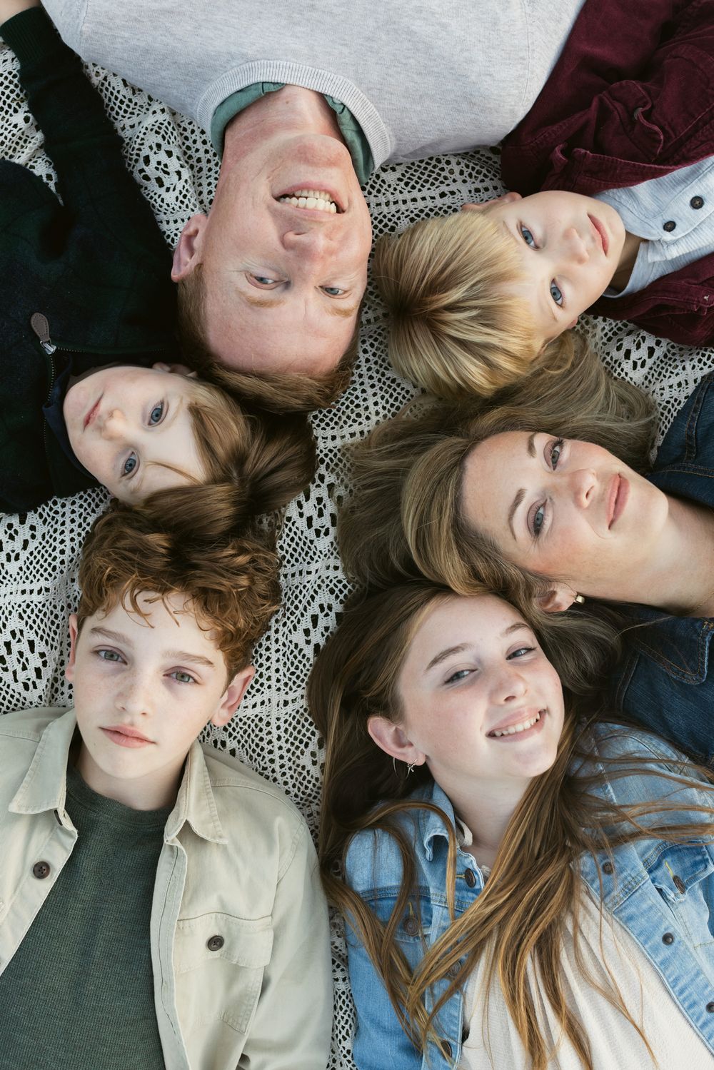 An above eye view of a family wearing fall colors lays on a cream crochet blanket for family photos in Seacoast area New Hampshire.