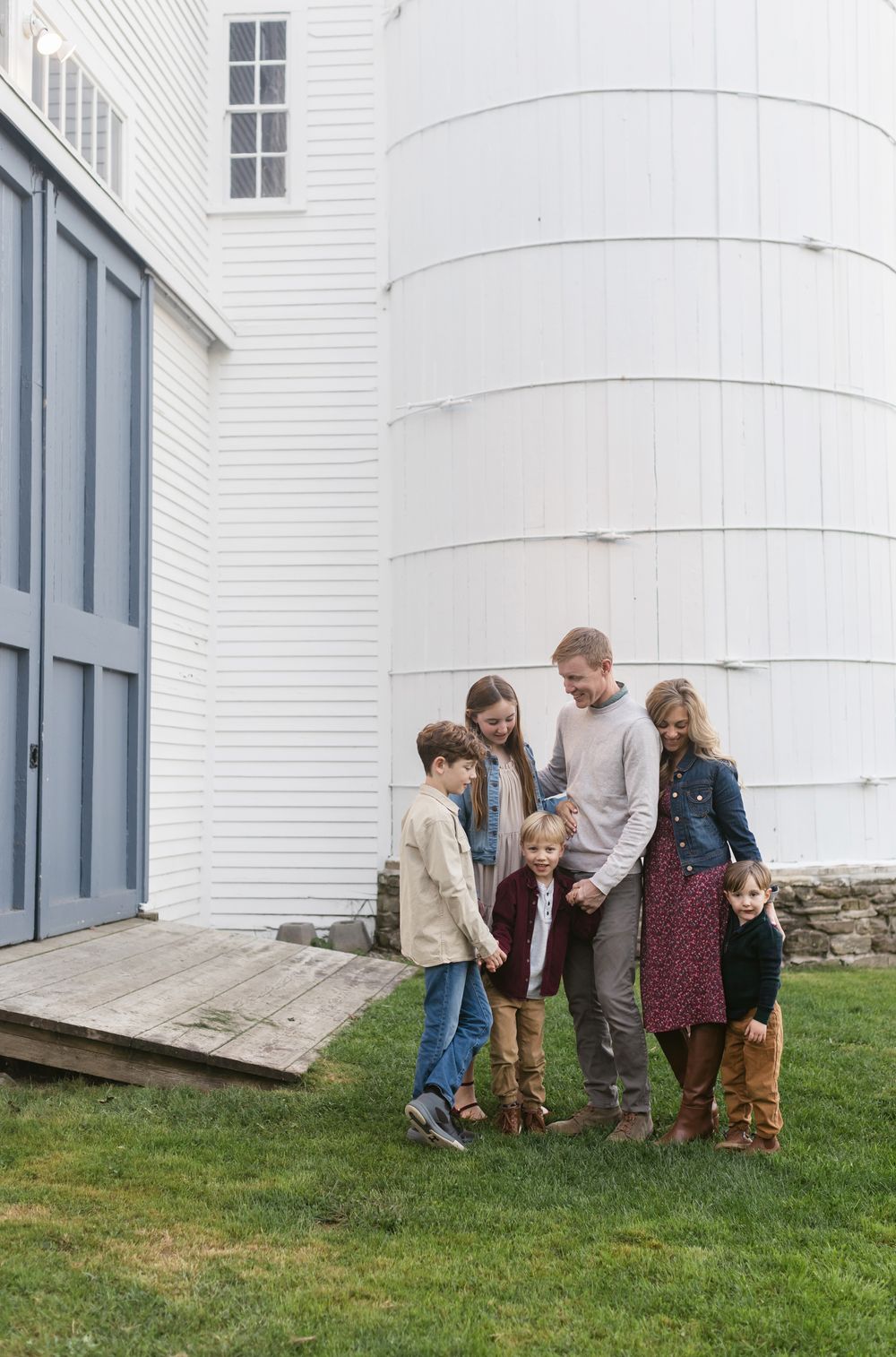 A family wearing fall colors poses in front of a white barm with a pale blue door at Saltonstall Farm in Stratham, New Hampshire.