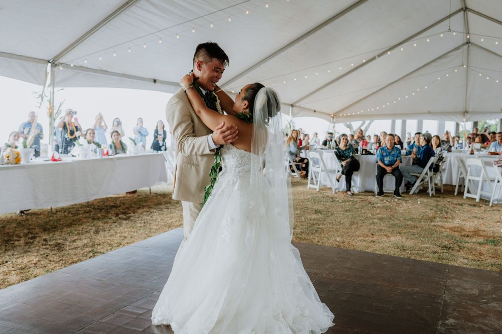 A couple shares their first dance at a wedding reception under a white tent with guests watching.