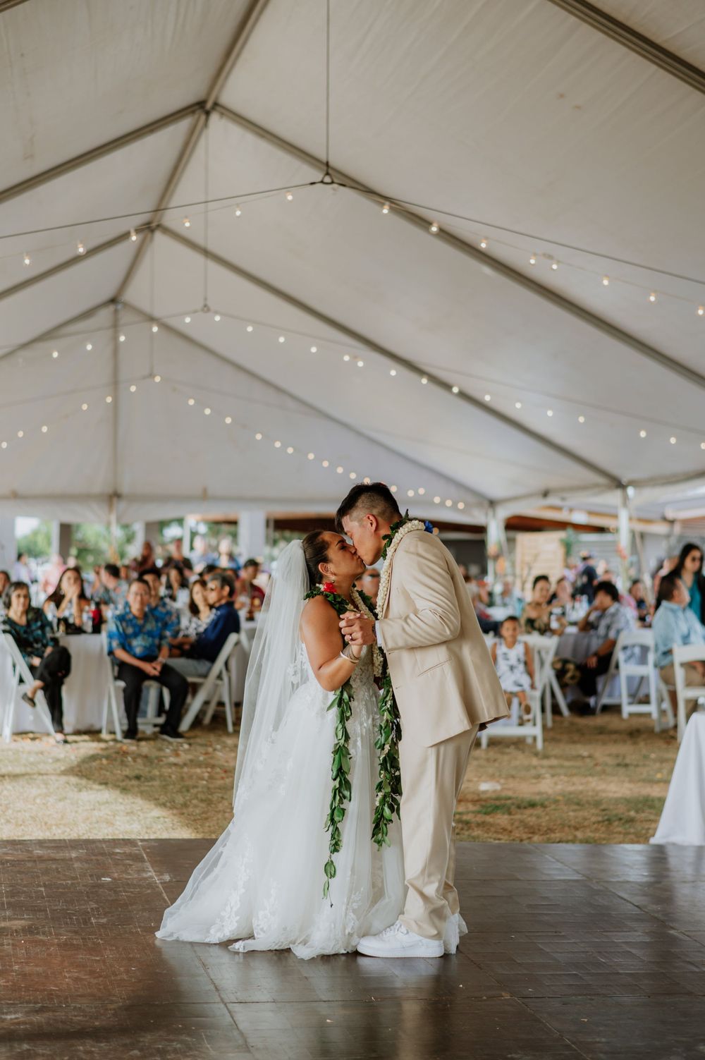 Newlyweds dance intimately during their reception under string lights in an outdoor tent venue.