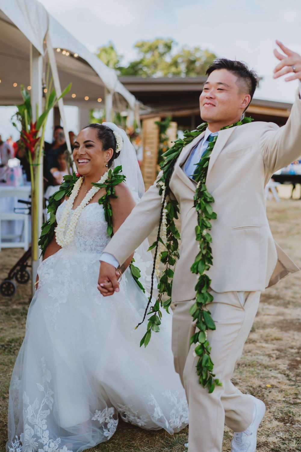 Newlyweds dancing and celebrating at outdoor reception wearing traditional Hawaiian greenery.