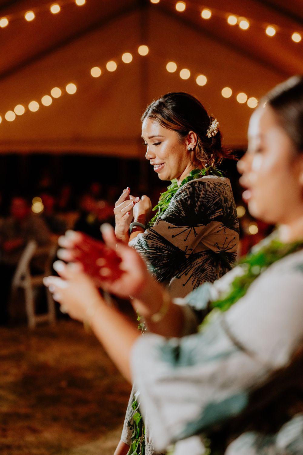 Wedding party members dance in formation wearing tropical leis under string lights.
