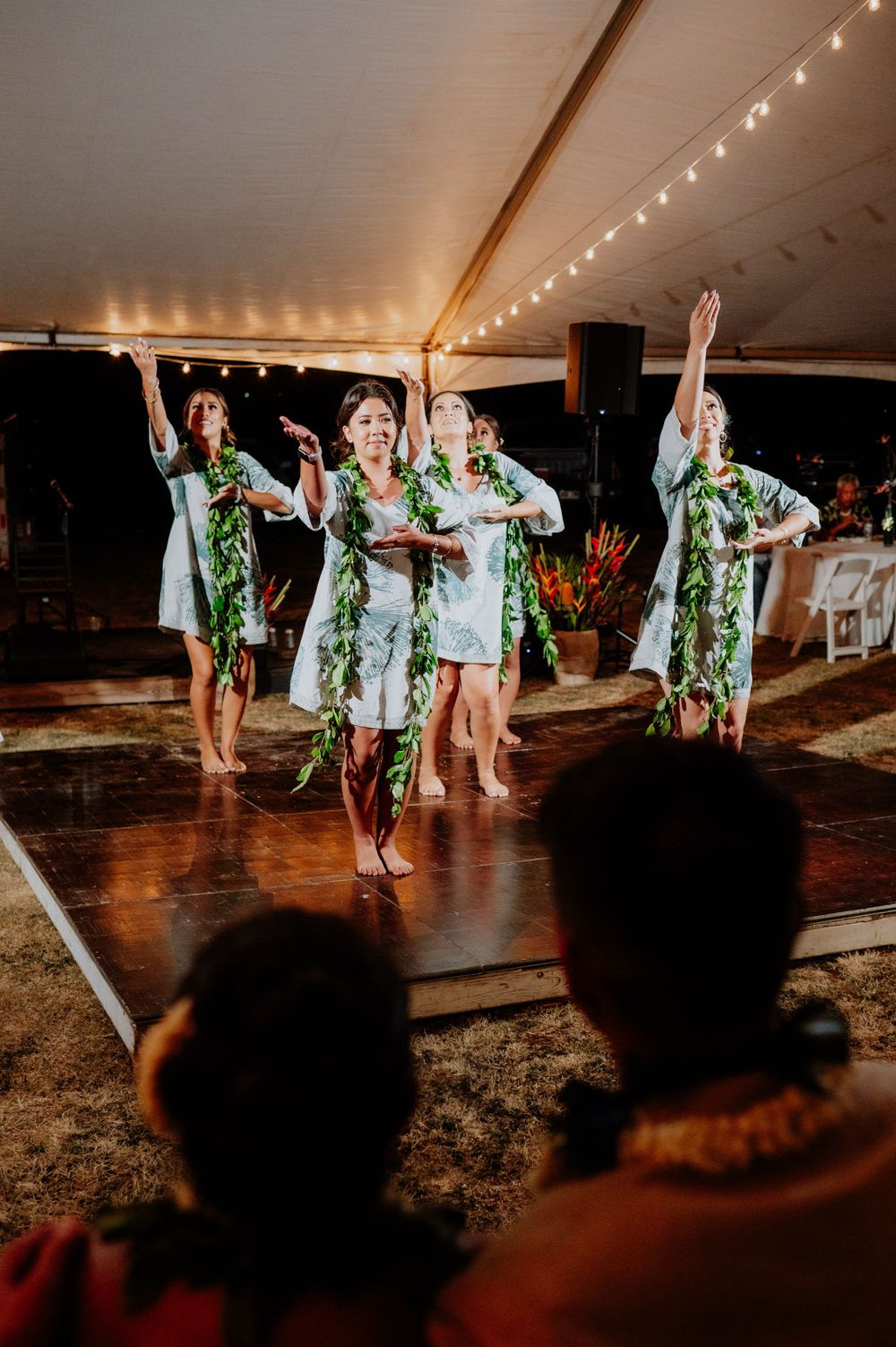 A group performs a synchronized dance routine wearing green leis at a wedding reception.