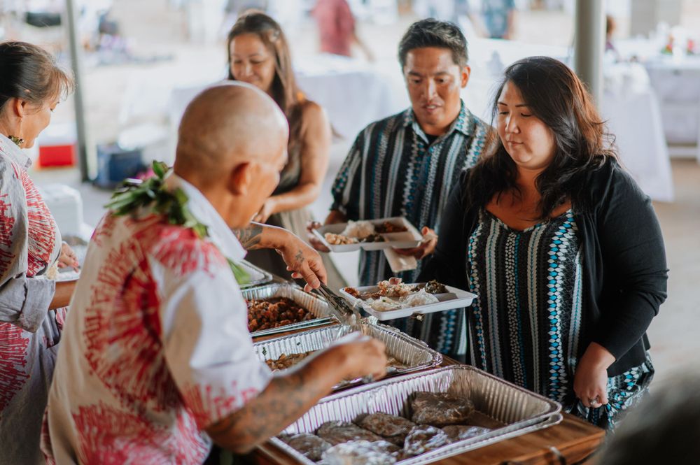 Guests serve themselves from buffet trays at an outdoor wedding reception.