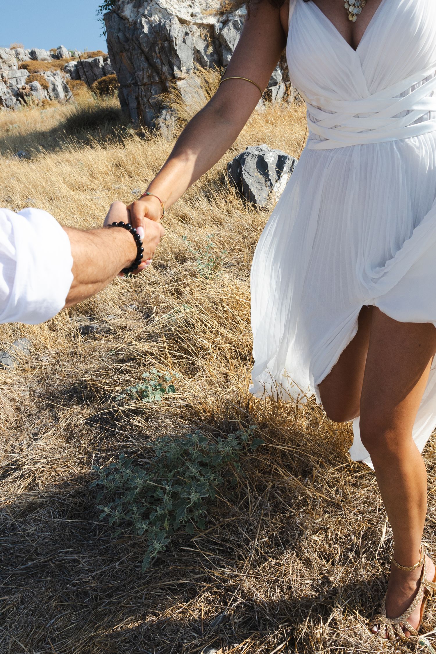 Close-up view of bare feet in dry grass wearing delicate white dress on a sunny summer day.
