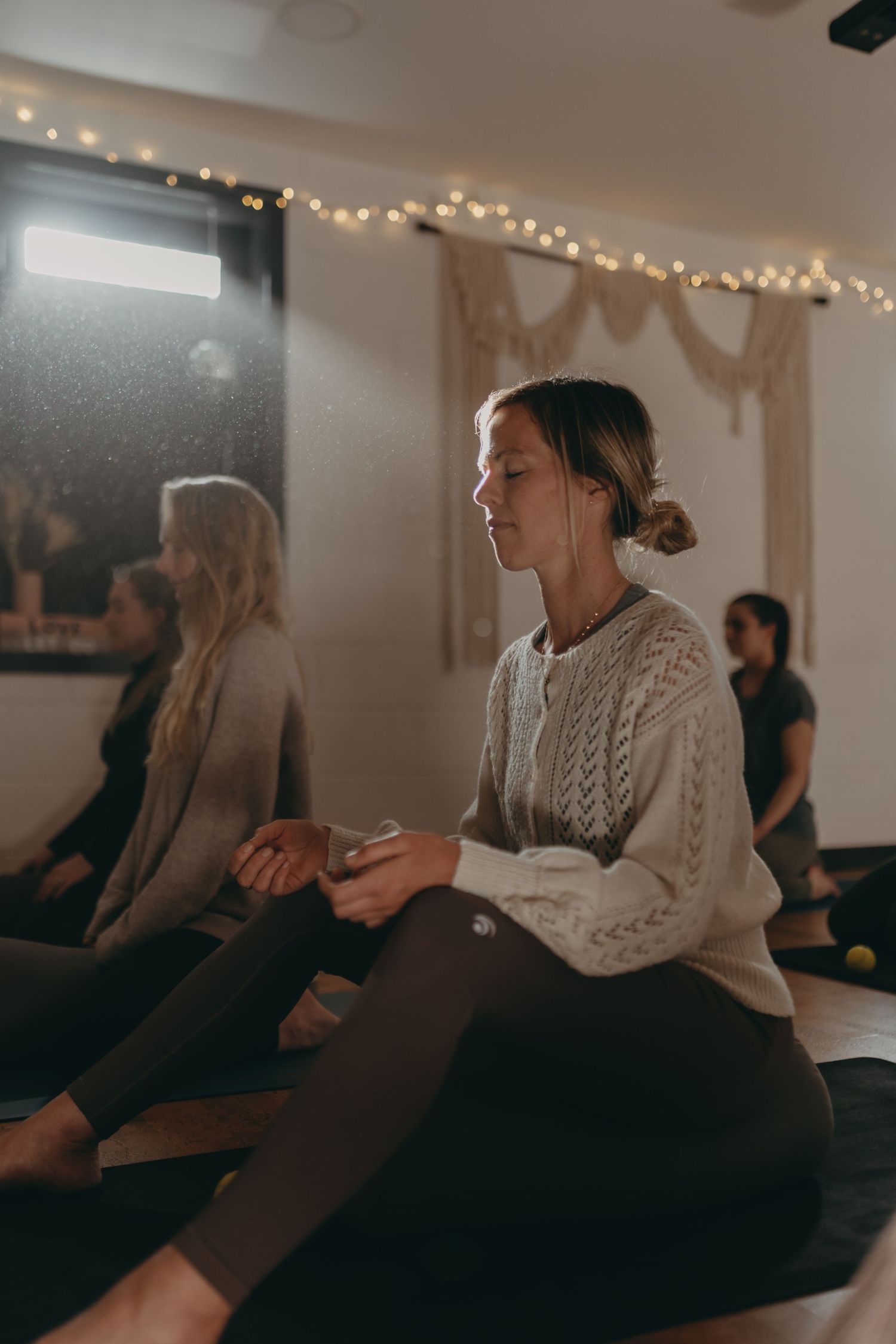 A person performs a series of stretching exercises on a yoga mat in a minimalist studio space with white walls and wooden floors.