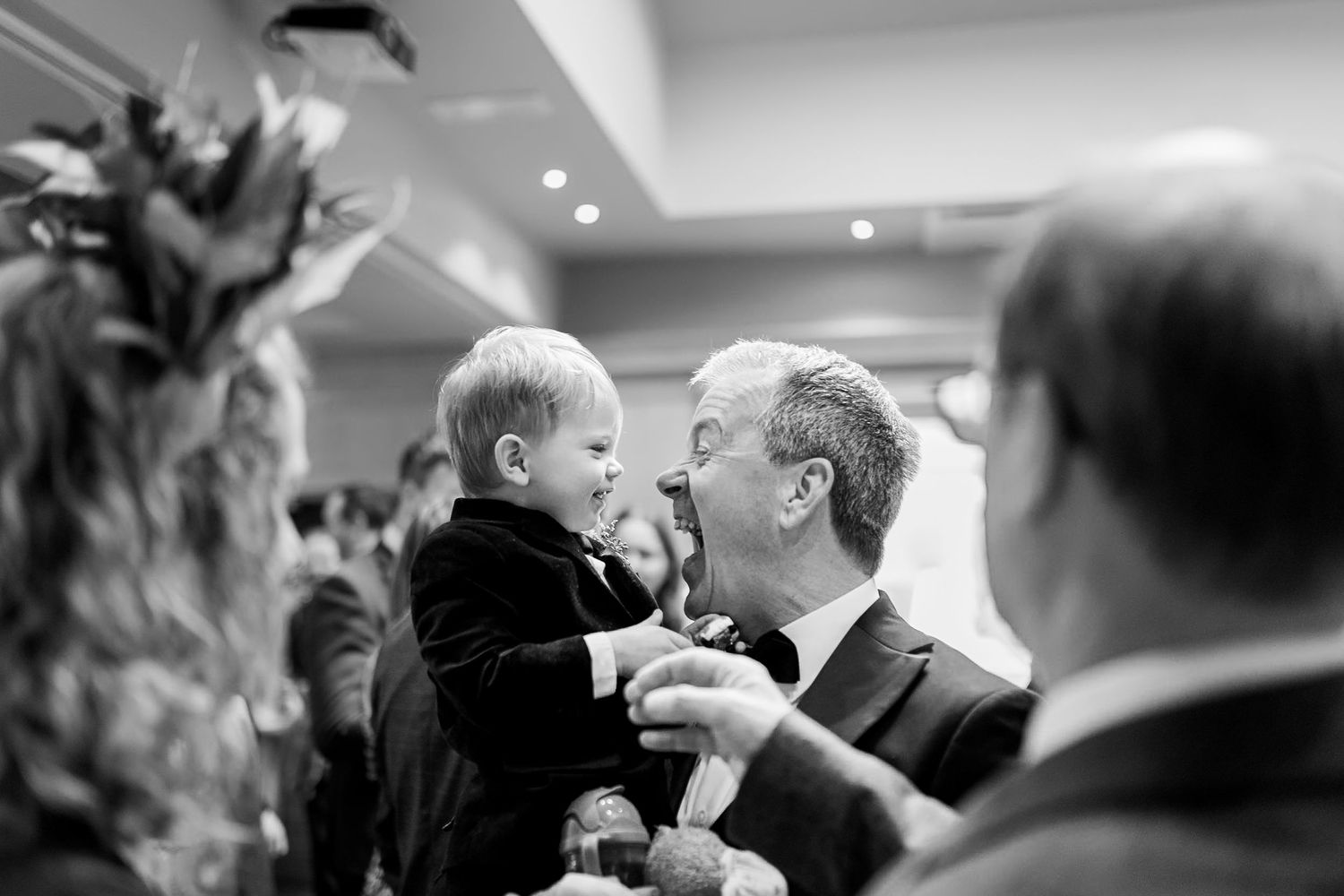 A sweet candid black and white moment captured between a person and a small child at an indoor gathering.