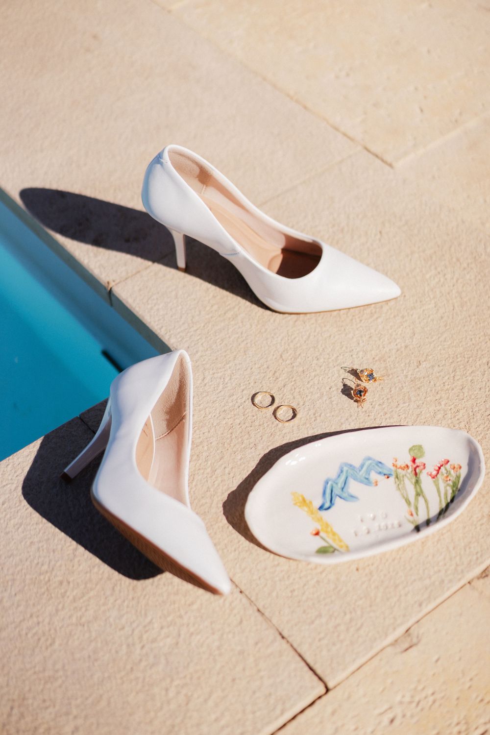 White bridal shoes with delicate embroidered details cast shadows on a light colored surface.