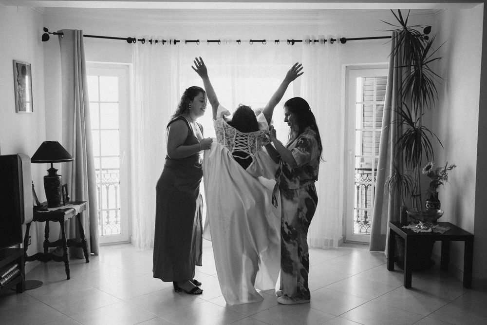 Three people celebrate in a bright room with French doors, captured in black and white photography.