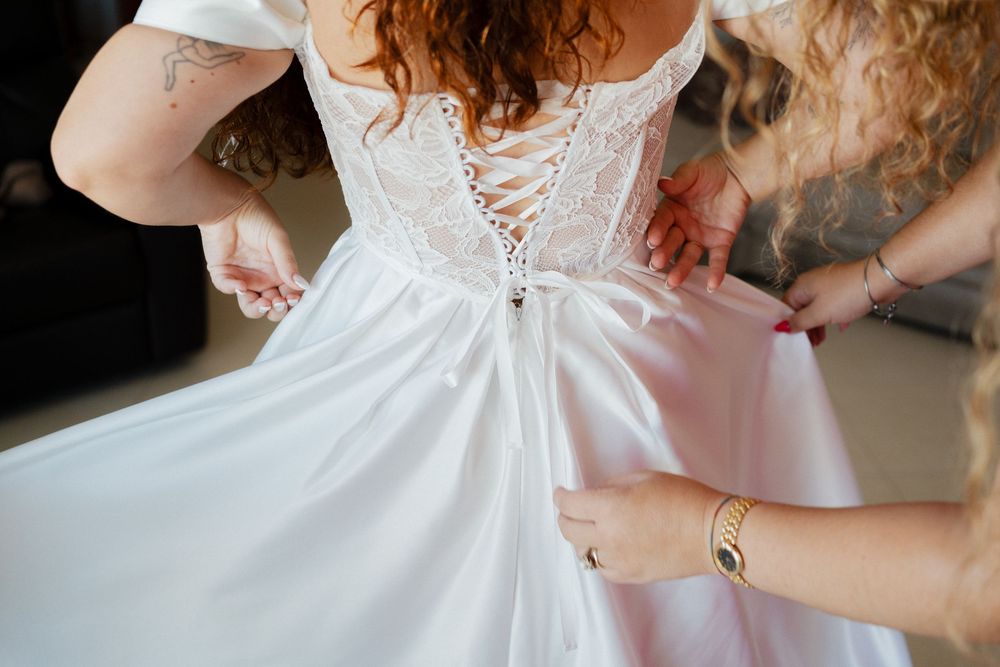 Close-up details of a white lace wedding dress being adjusted and fitted.