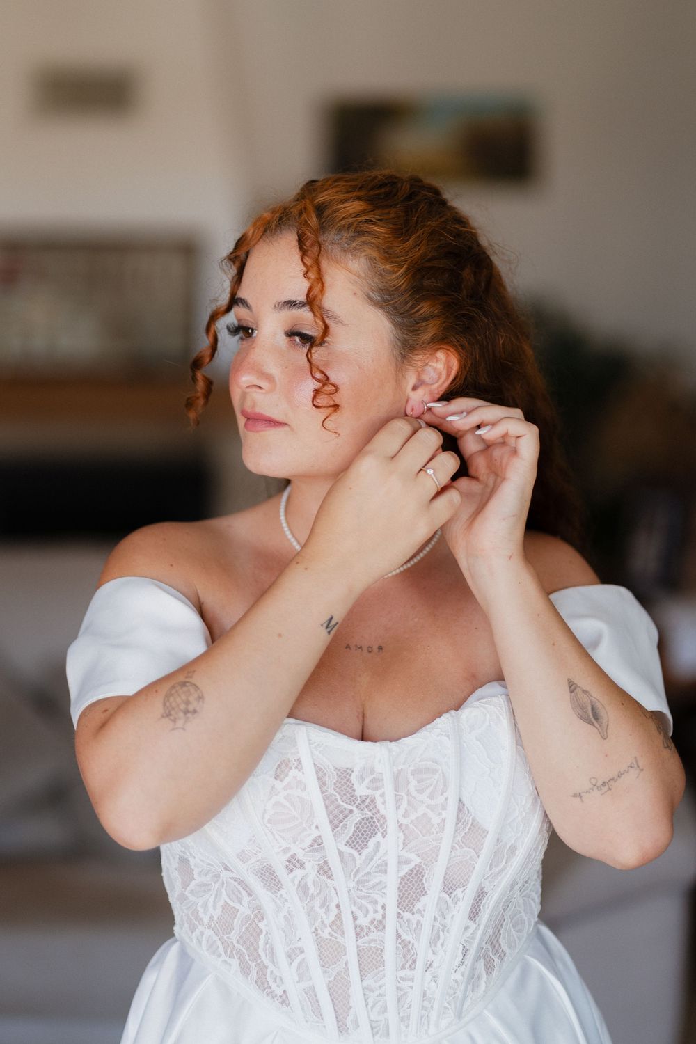 Close-up of someone putting on delicate earrings while wearing a white lace dress.
