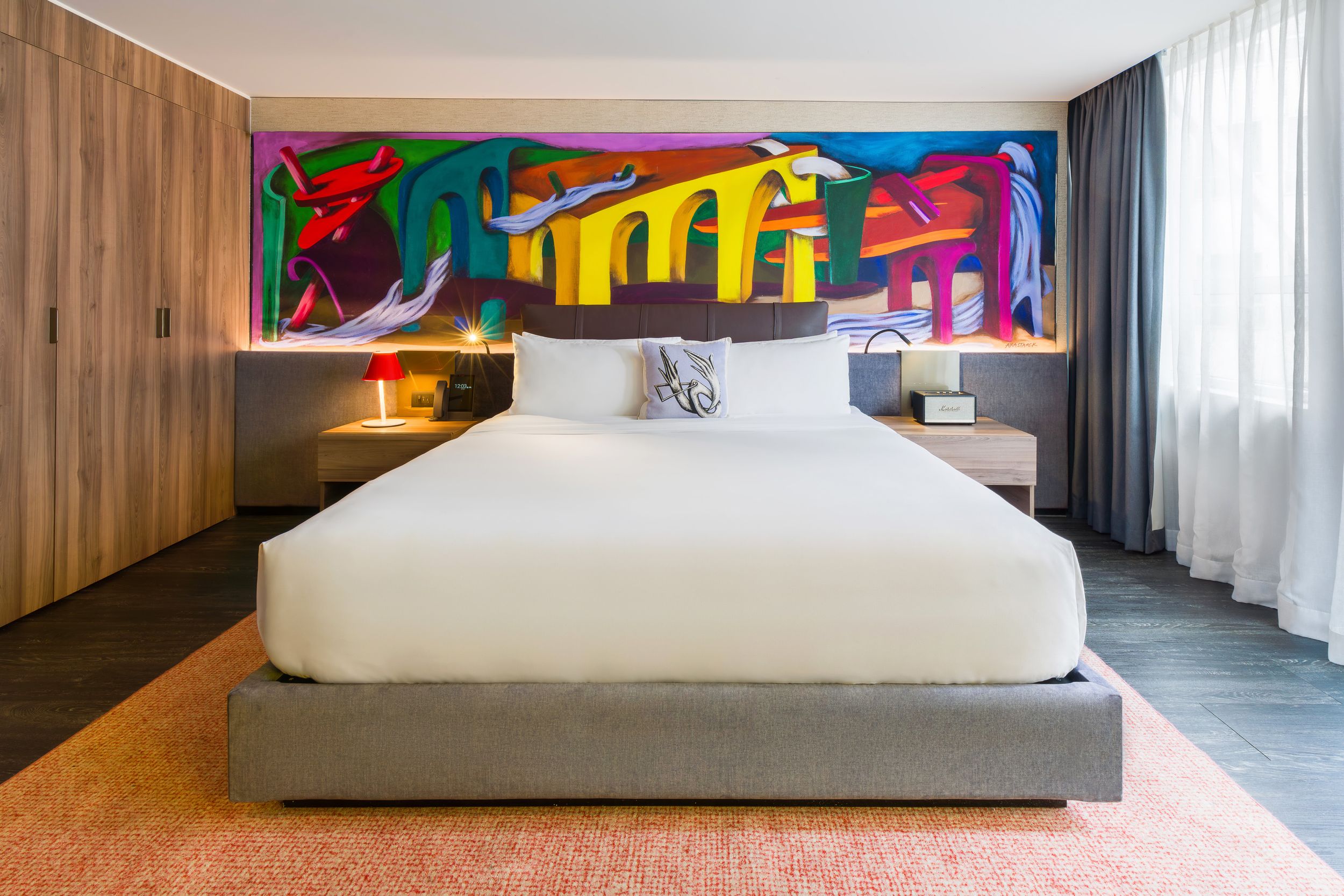 Modern bedroom interior with wood paneled walls, white bedding, and colorful abstract artwork on display.