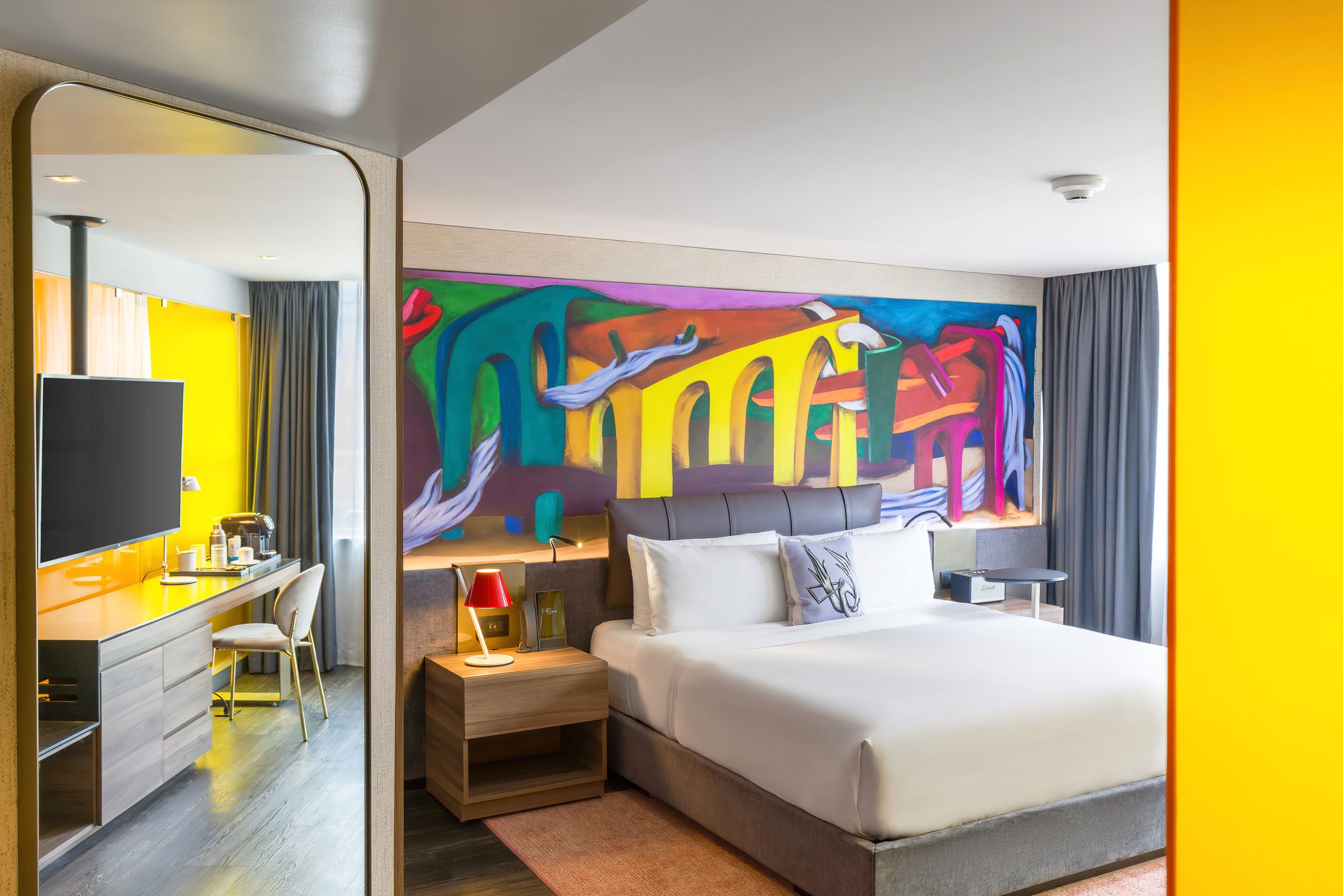 Vibrant hotel bedroom with yellow accent walls and colorful mural artwork creating a dynamic atmosphere.
