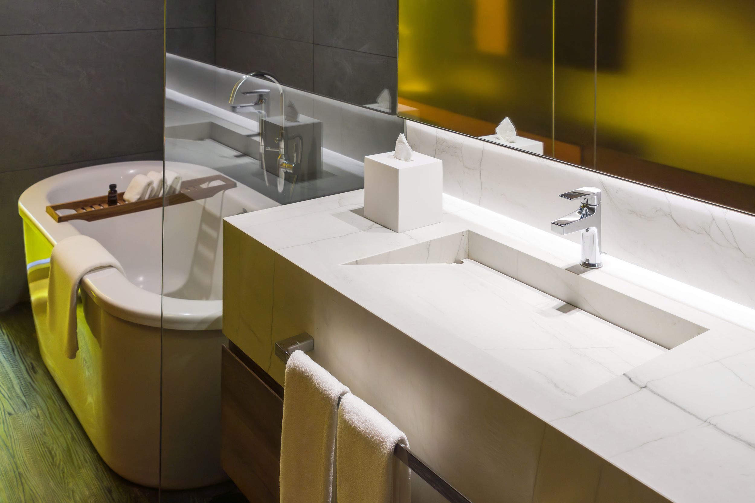 Long white bathroom vanity with integrated sinks illuminated by yellow accent lighting.