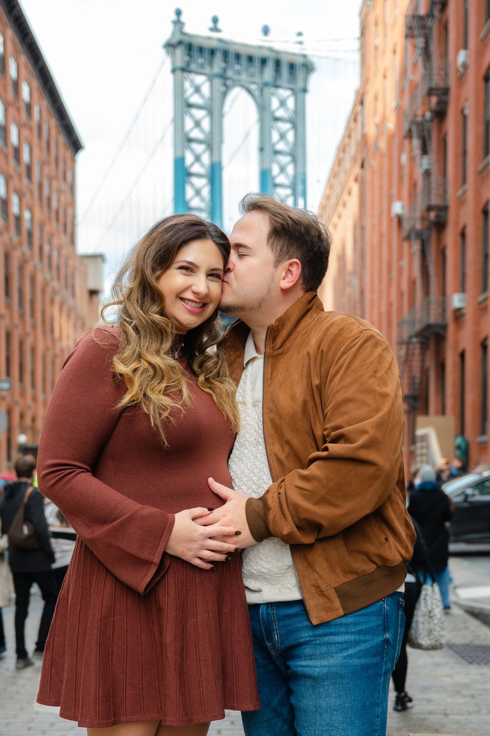 A couple shares an intimate moment on a Brooklyn street with the Manhattan Bridge in the background.