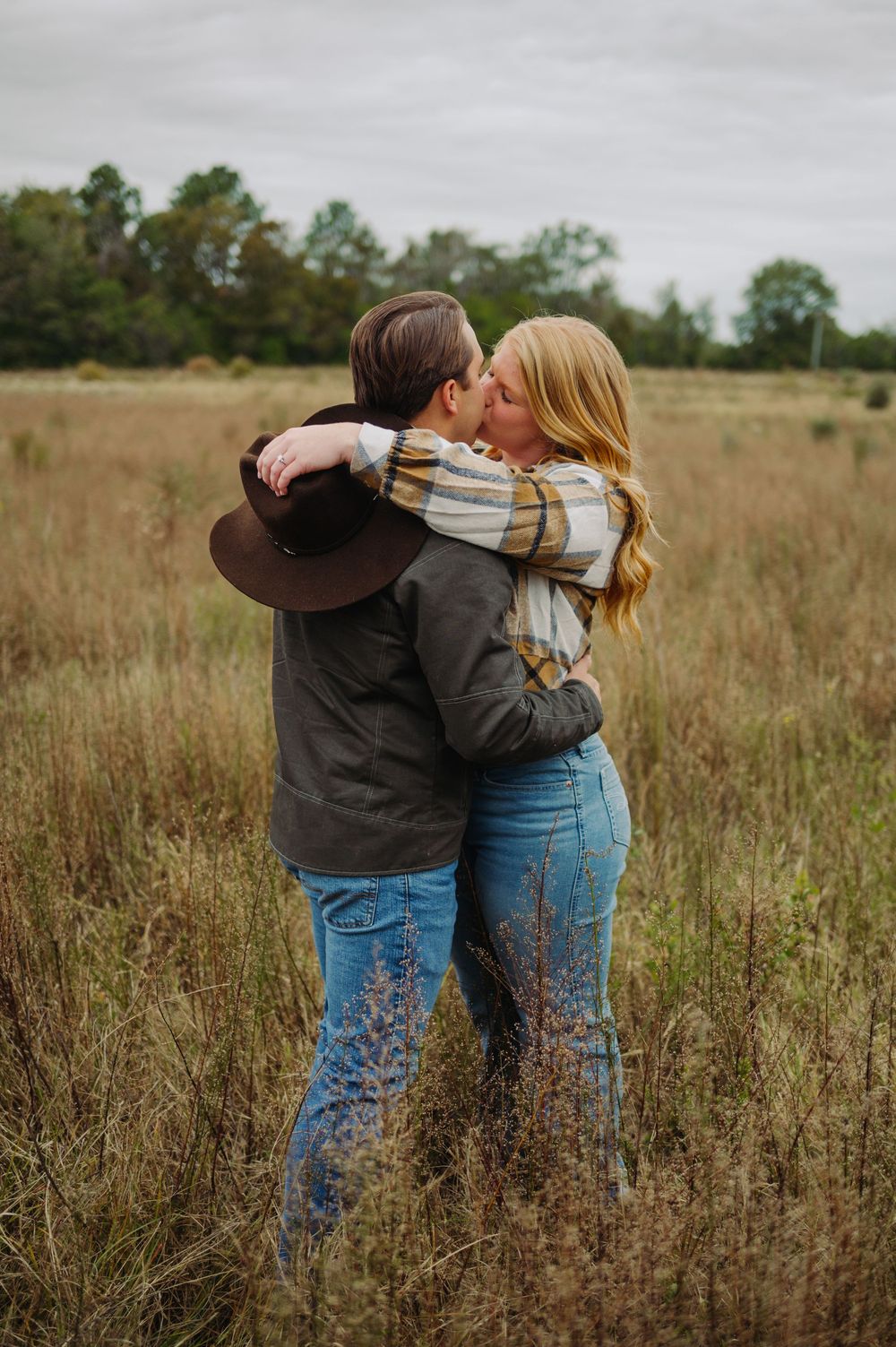 A couple shares an intimate moment in a golden field while wearing casual western attire.