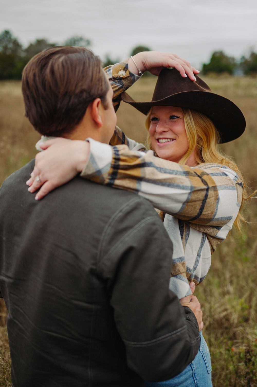 A couple embraces in a romantic moment outdoors in a rustic field setting.