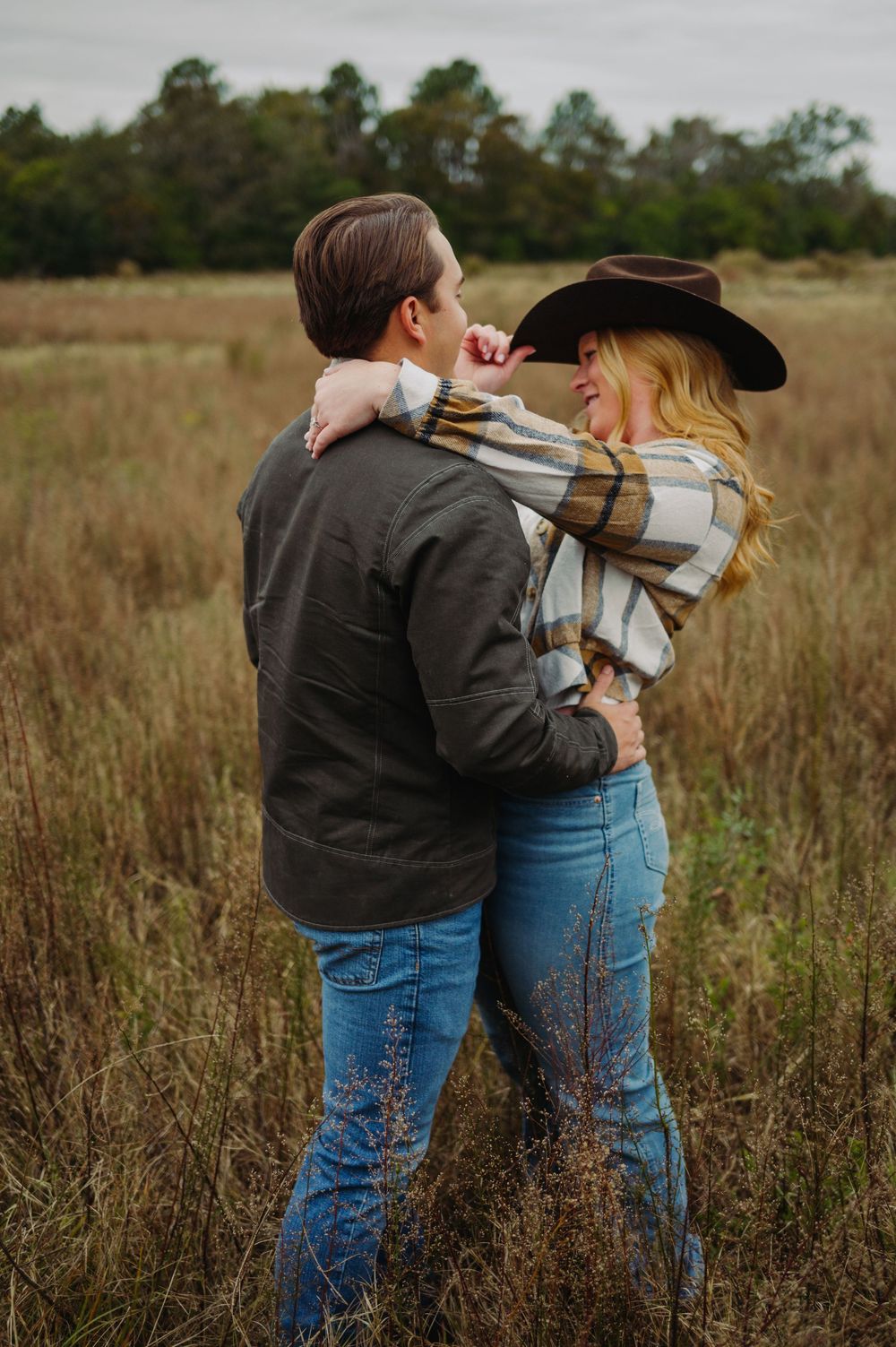 Couple in casual wear sharing an intimate moment in a rustic field during golden hour.