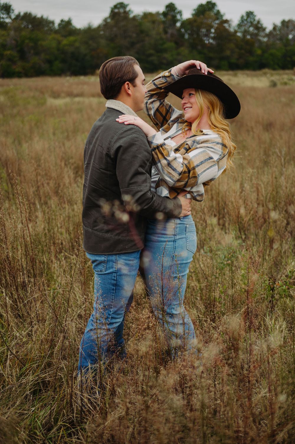 A couple embraces in a rustic fall field setting with western style clothing and hats.