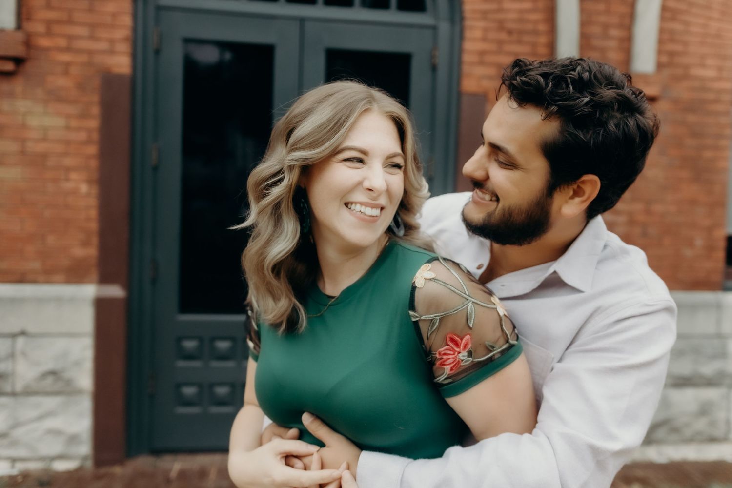 Couple sharing romantic moments against brick building exterior.