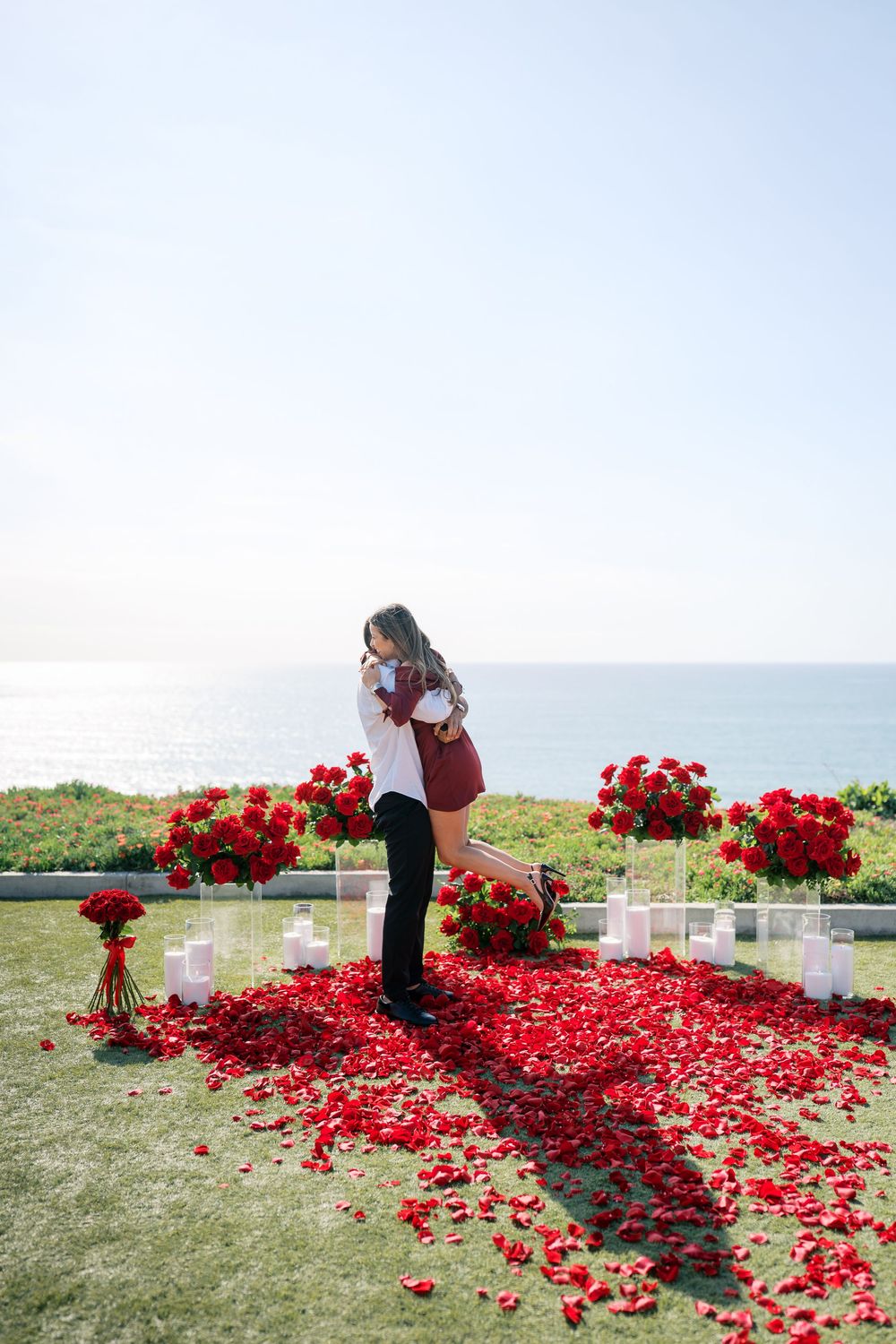 A couple sharing a special moment among scattered red rose petals and white crosses by the sea.