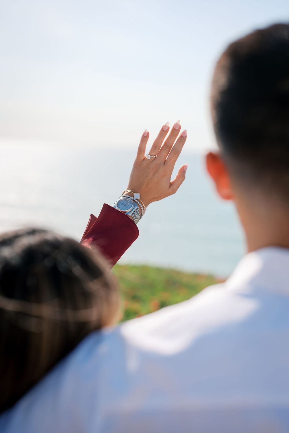 Close up of a hand displaying an engagement ring against blue sky background.