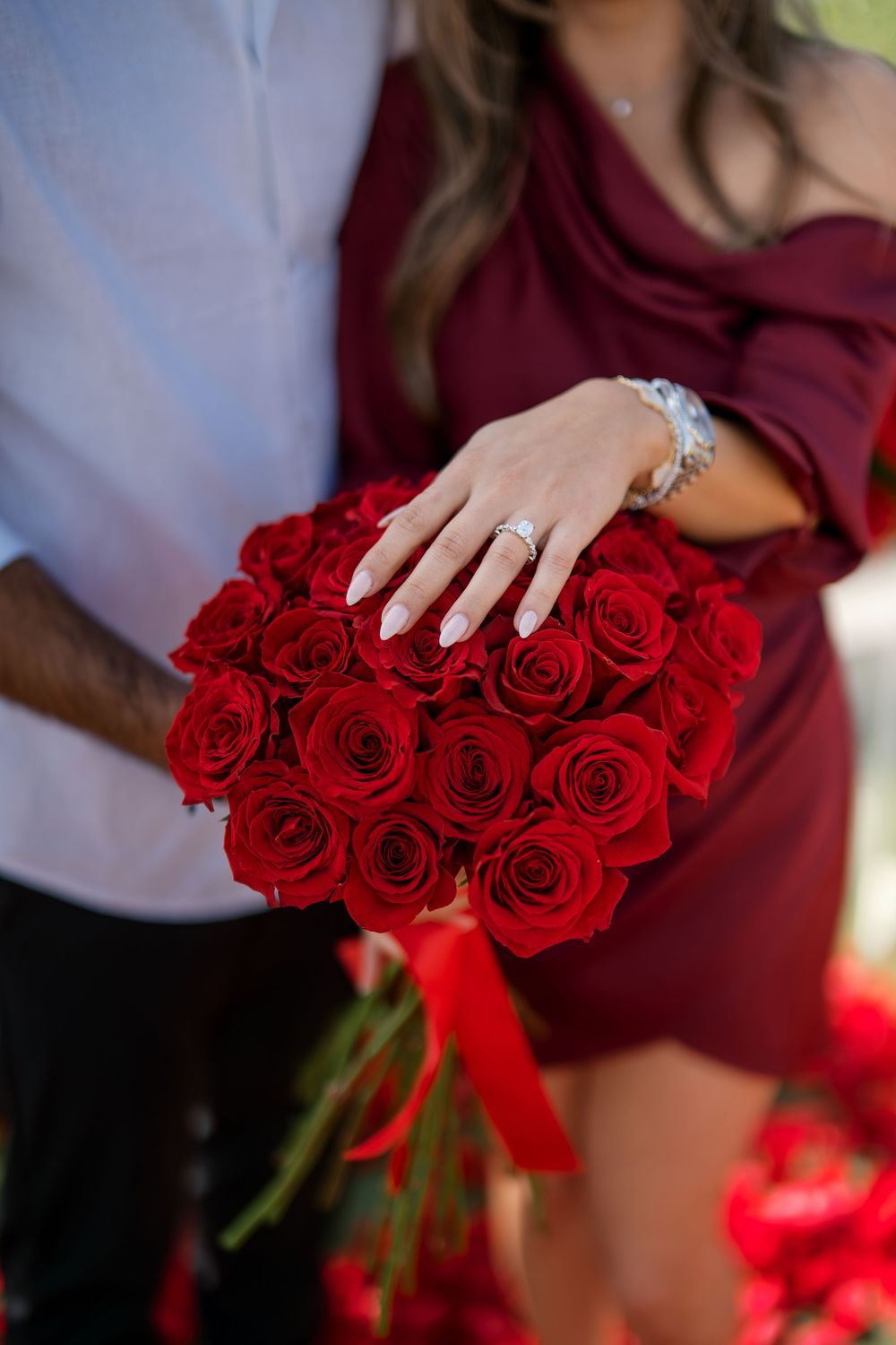 Close up of red roses bouquet with burgundy ribbon held against burgundy dress.