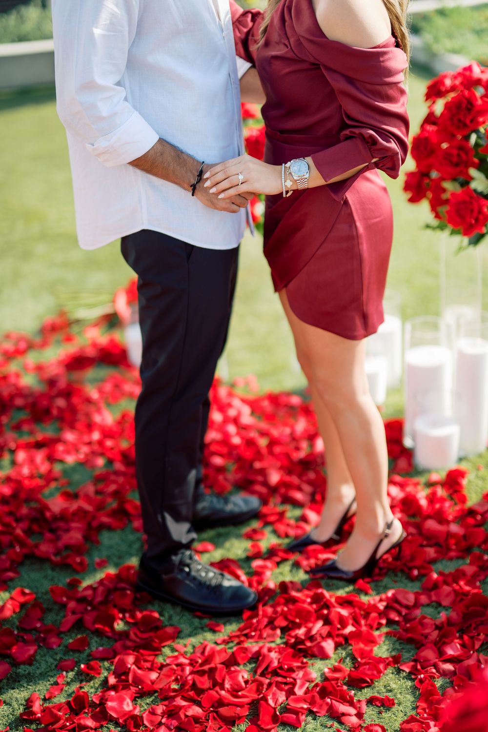 A couple stands together on scattered red rose petals during a romantic photoshoot.