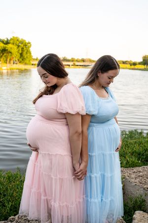 Two friends in pastel dresses posing by lakeside at sunset.