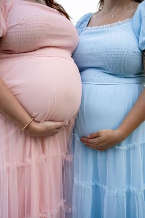 Two people in pink and blue tulle dresses showing their baby bumps in a maternity photoshoot.