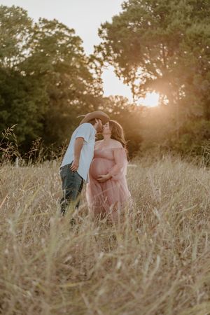 Couple poses lovingly in tall grass during golden hour sunset photoshoot.