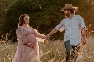 Couple shares intimate moment in field wearing pink dress and western attire.