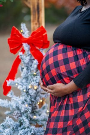 Holiday maternity photos with buffalo plaid dress and flocked Christmas trees.