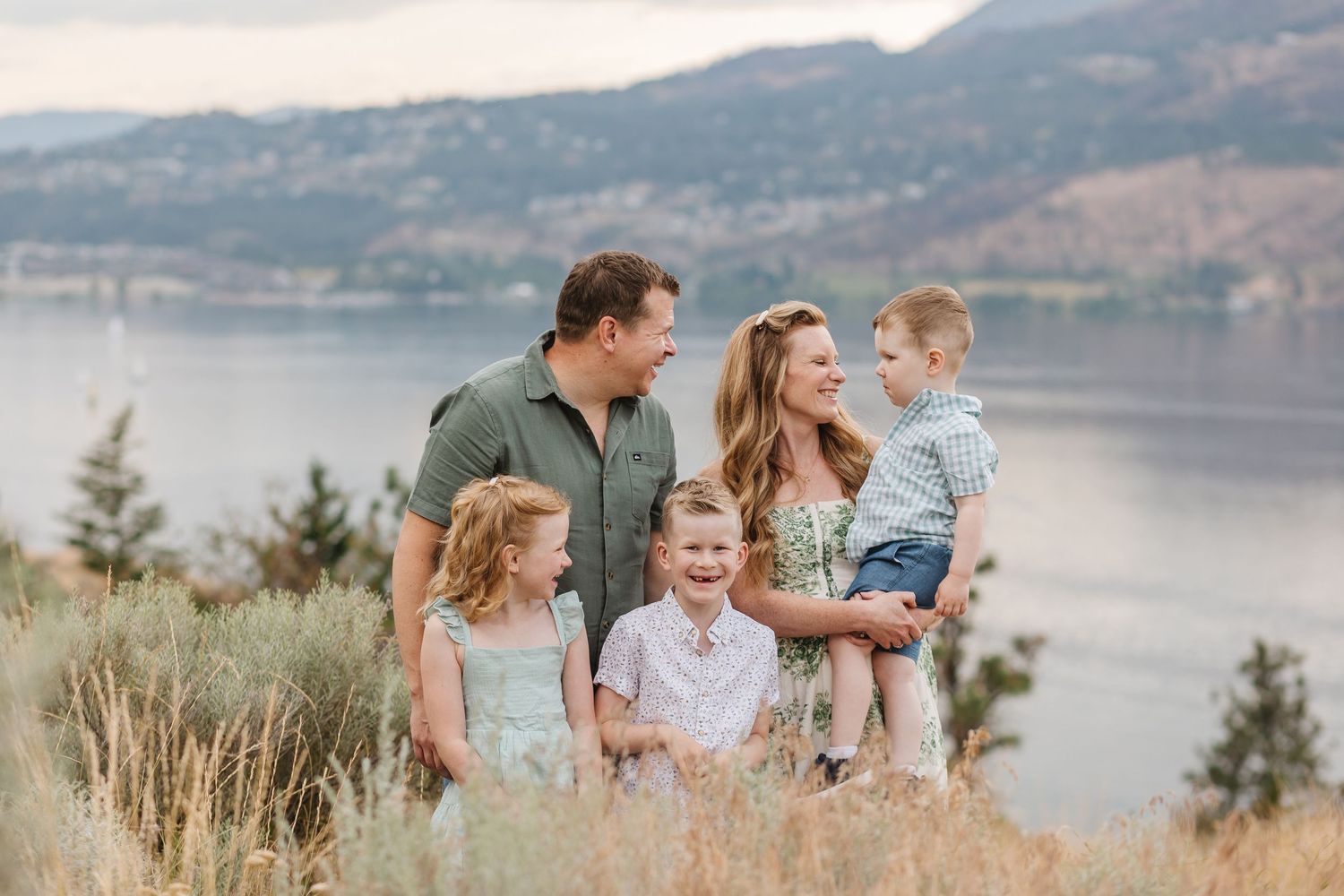A family enjoys a scenic moment together on a rocky overlook with mountains and water in the background.
