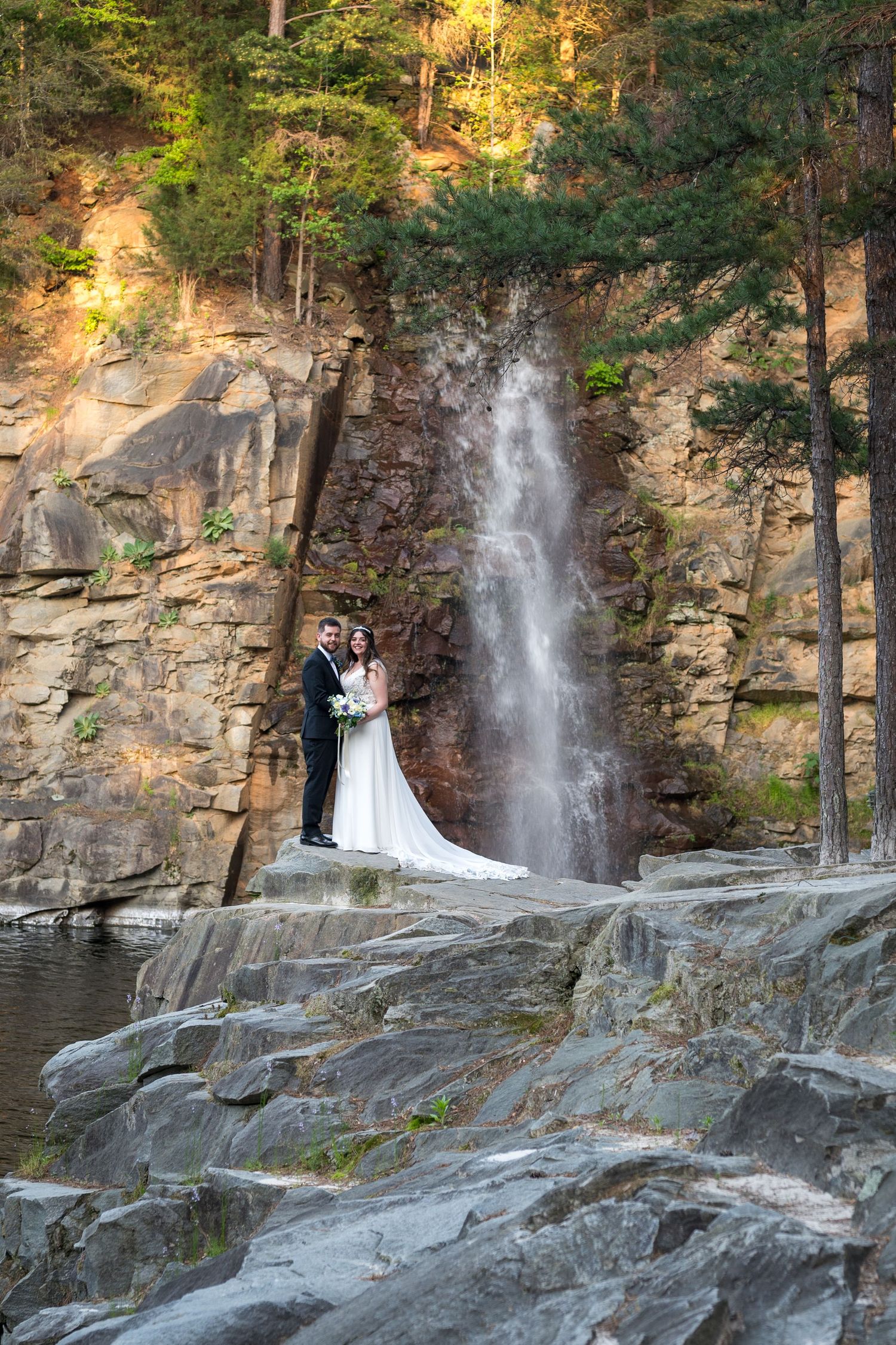 A joyful celebration outdoors with people gathered around a red floral backdrop in a park setting.