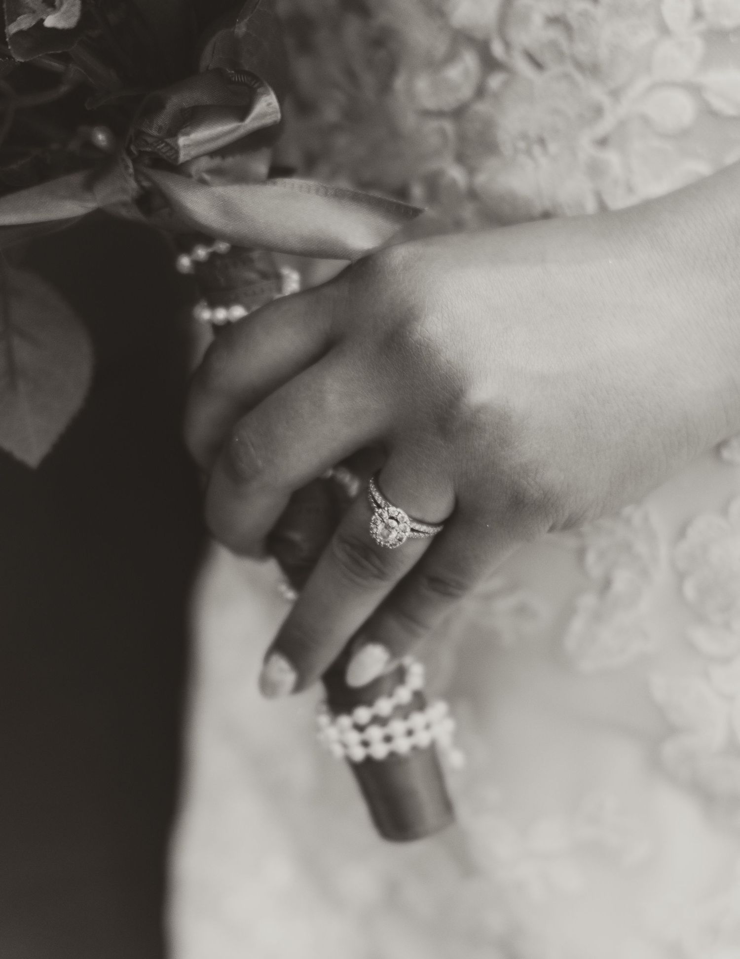 Black and white detail shot of bride's hand showing engagement ring and pearl bracelet.