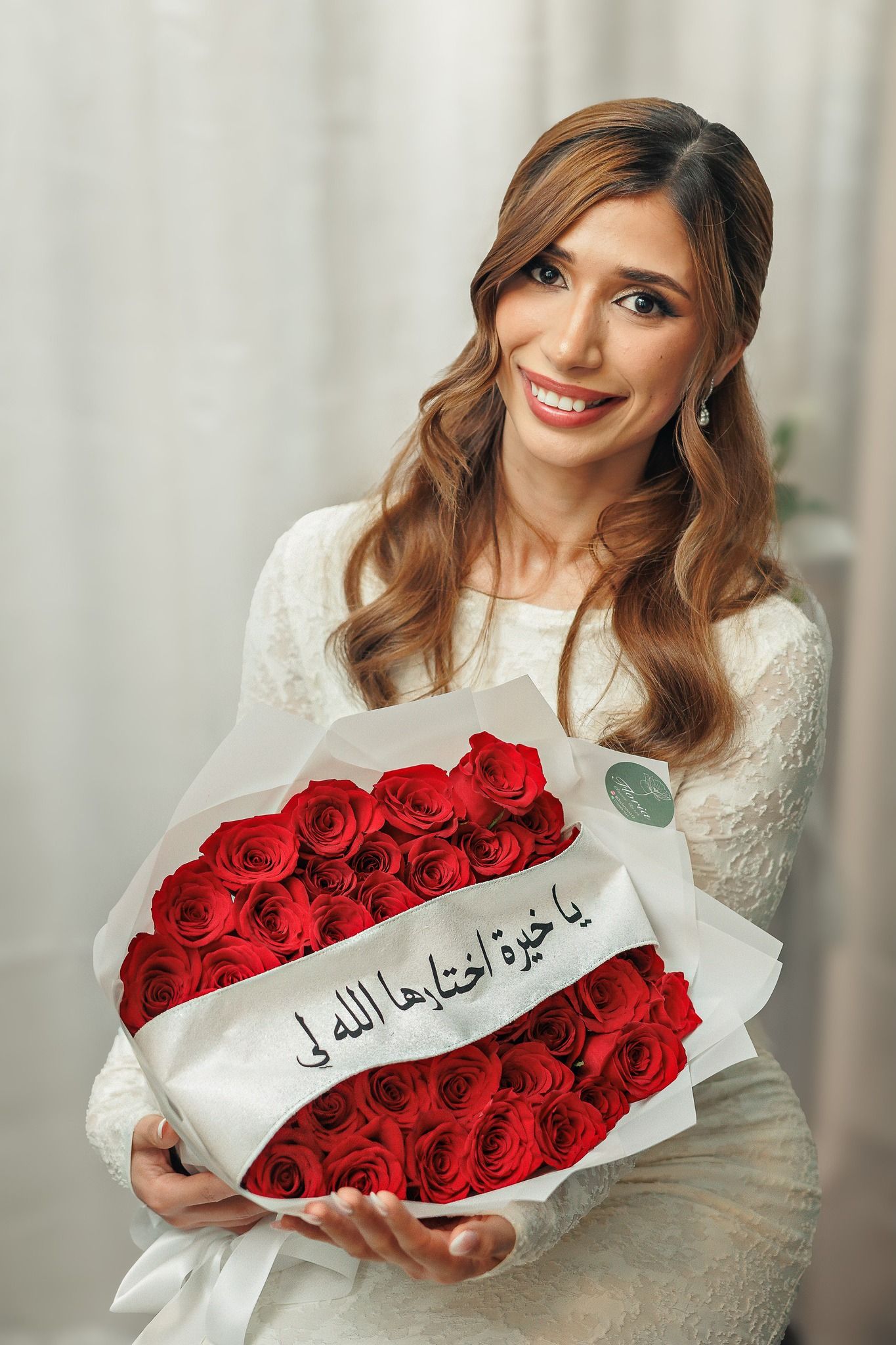 Elegant white lace dress with vibrant red roses arranged in a decorative display against light curtains.