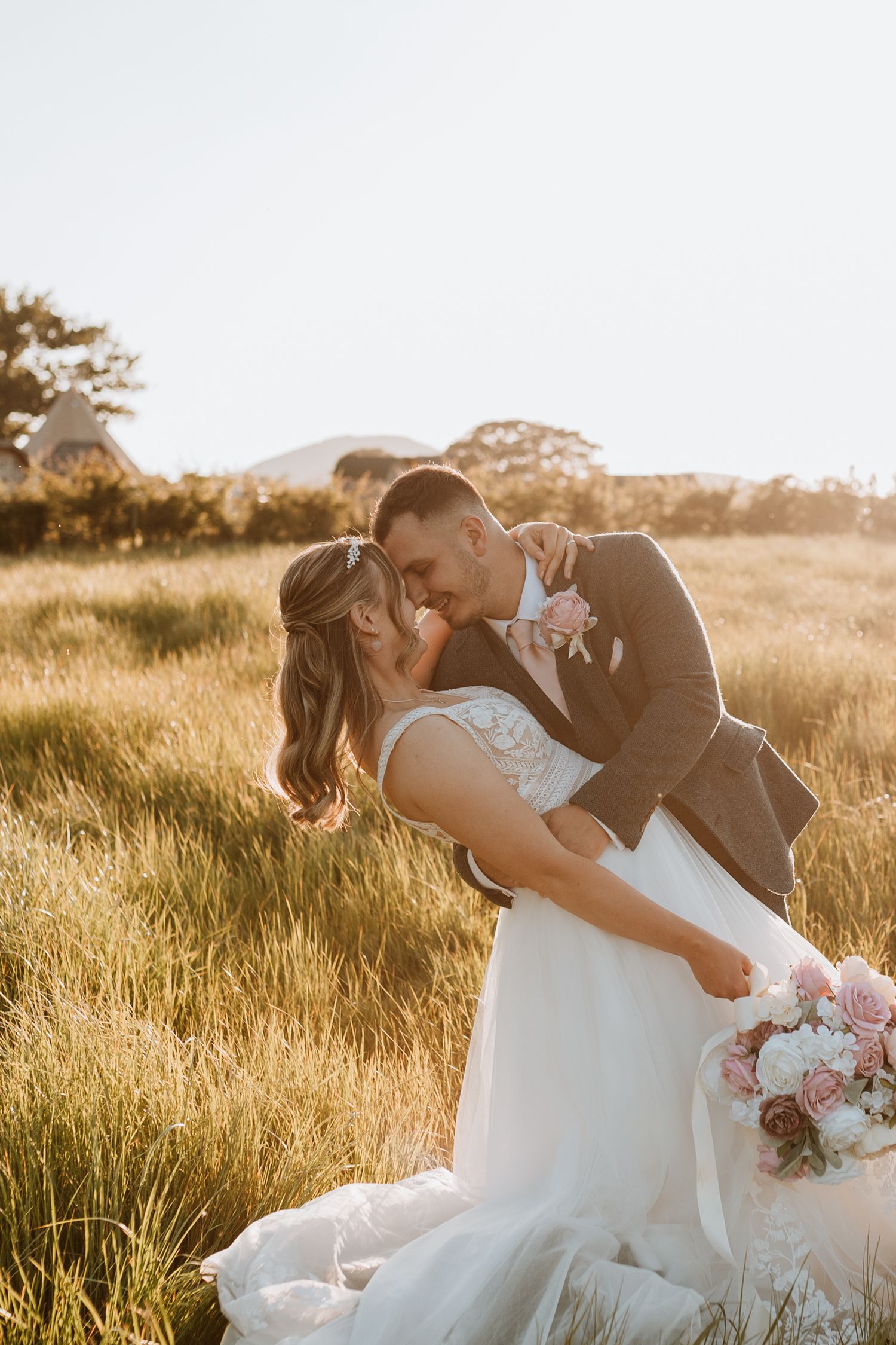 A romantic sunset wedding photo series shows a couple embracing in a golden field of tall grass at Stanford Barns