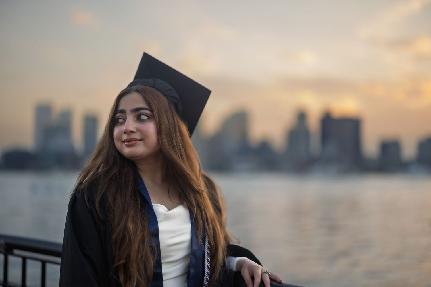 Person in white sweater enjoying sunset views of city skyline from waterfront during golden hour.