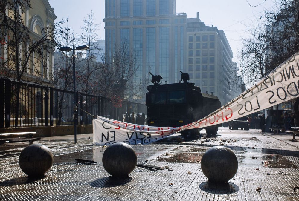 Street scene following a demonstration with tattered banners and a police water canon vehicle after a protest . Santiago, Chile