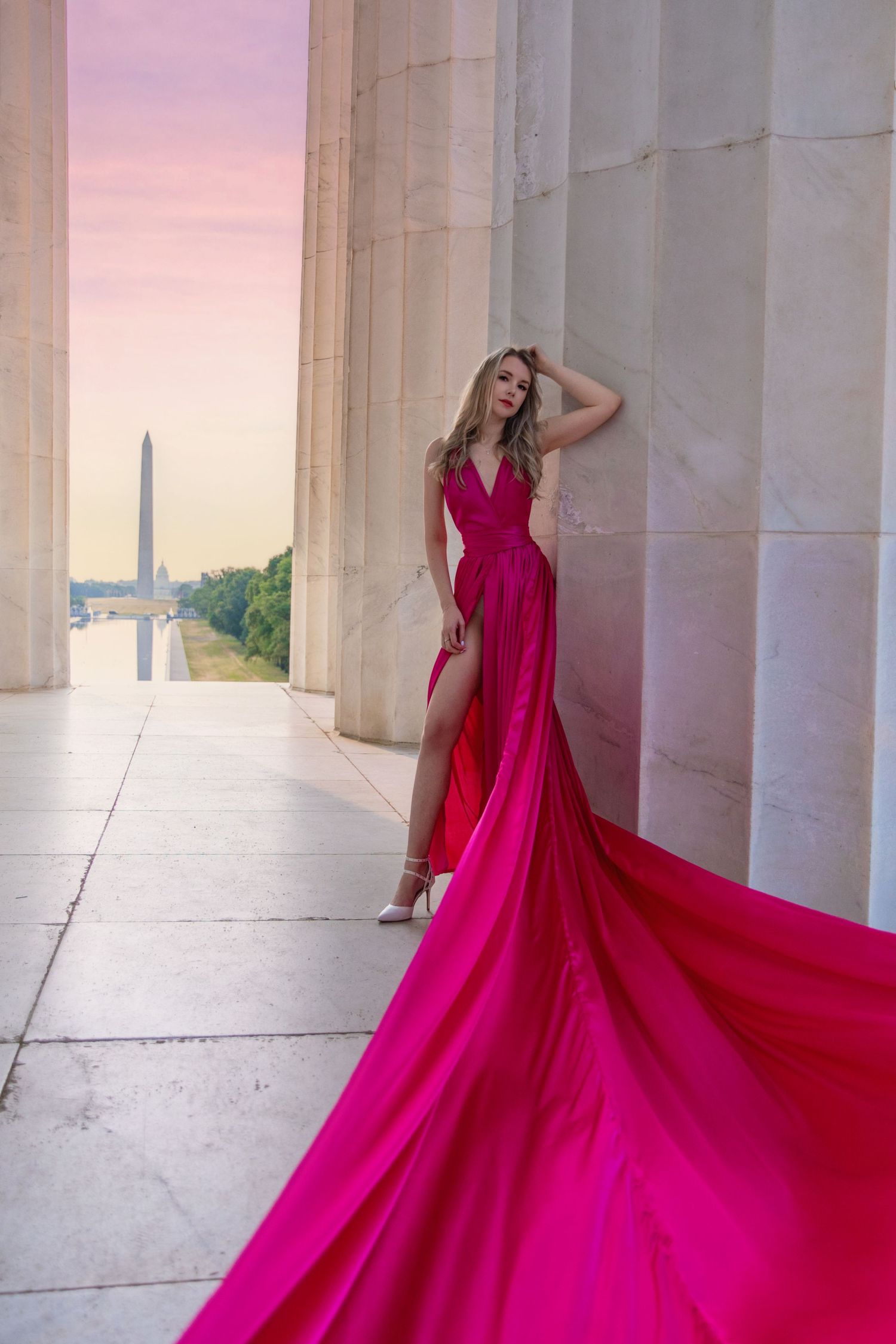 A couple poses among classical columns while a flowing dusty rose gown billows dramatically in the breeze. Washington DC Engagement photos