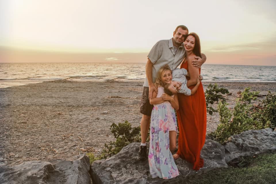Family photoshoot at sunset on a rocky beach with warm golden lighting.